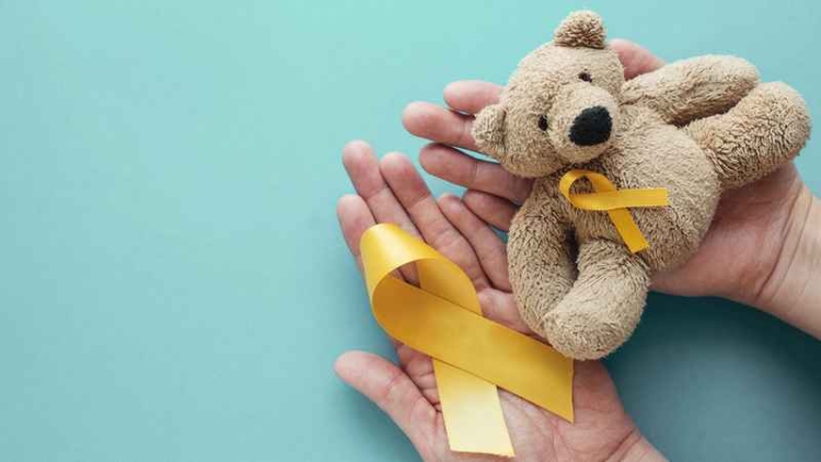 Hands holding children soft toy brown bear with yellow gold ribbon, Childhood cancer awareness